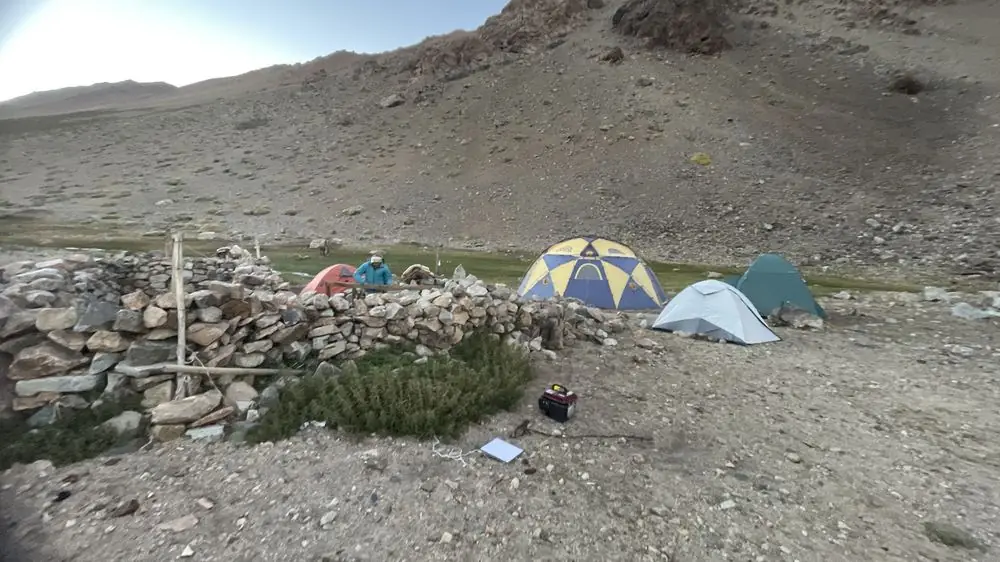 Campamento de exploración con carpas y generador junto a un corral de piedra en la cordillera