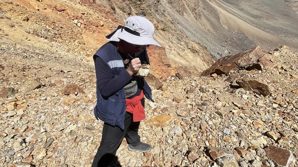 Geólogo examinando una muestra de mano con lupa sobre una ladera de roca alterada