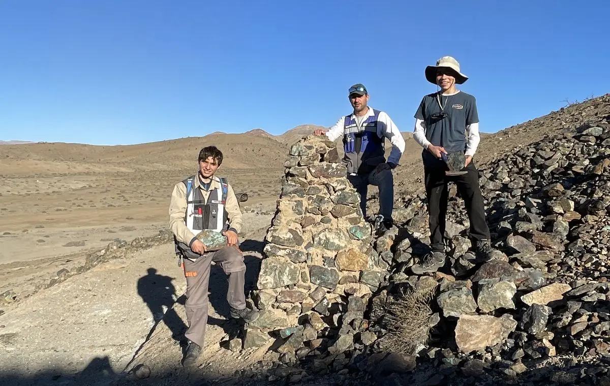 Tres integrantes del equipo en terreno junto a un hito de piedra levantado con roca mineralizada, con la pampa de Atacama de fondo